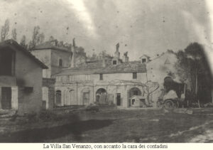 Fotografia storica in bianco e nero di Villa San Venanzo con la casa dei contadini annessa. La villa, immersa nel paesaggio marchigiano, presenta un'architettura rurale caratteristica, con archi e strutture in muratura.